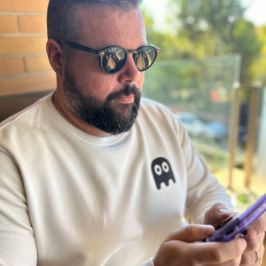 Hombre sentado con gafas de sol jugando a videojuegos con la sudadera de algodón orgánico color beige de Julieta Jaleo con fantasma negro en pecho izquierdo