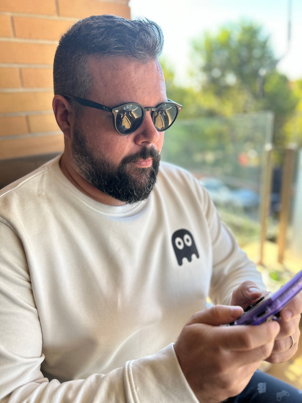 Hombre sentado con gafas de sol jugando a videojuegos con la sudadera de algodón orgánico color beige de Julieta Jaleo con fantasma negro en pecho izquierdo